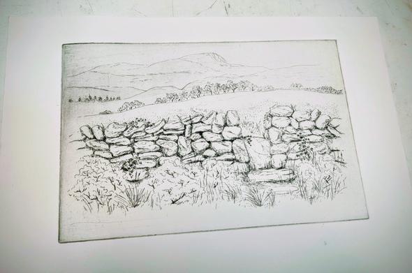 A black ink test print of an etching depicting a stone wall with a stile in the foreground and a field and mountains in the background.
