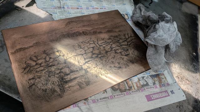 Photo of the plate during the inking process, showing the lines appearing clearly in black on the copper surface.