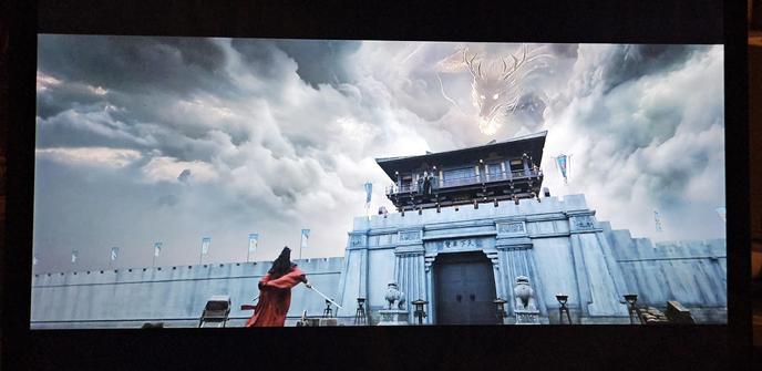 Su Mu Yu, in red hanfu, standing at the gate of the humungous Wushuang city wall. The wind blows through his clothes as he waits for the battle to start. Over the gate storm clouds are parting, as a white dragon sores down towards him.