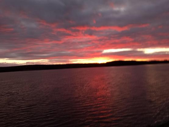 Looking across the harbour, the western sky is thick with dark clouds, the bottom of each in a strong pink shade, amplified by the reflection off the ocean below