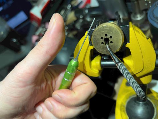 Photo of a vise that has a picked (you'll just have to trust me 🤣) Cavers iZiS in it. The lock has a weird L-shaped tension tool with a knurled handle still inside it, sticking out at a 45° angle from the bottom of the keyway. There's a hand giving a thumbs up and holding a green handle that has a pointy "probe" sticking out from it