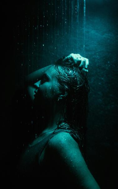 A person lit by a blue light standing in the rain.