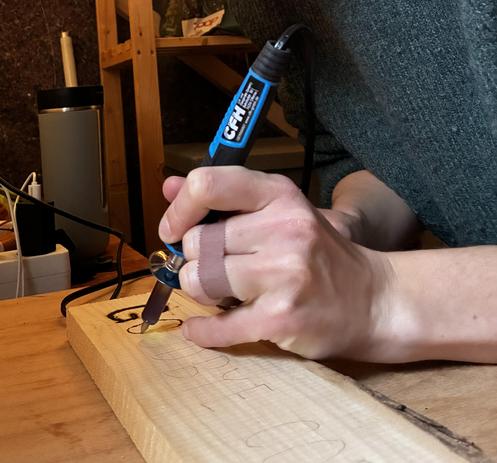Hond with soldering gun burning some letters in a piece of wood.