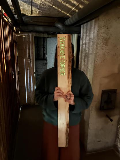 Person in dark hallway hiding behind a piece of wood that says "goodbye corner". The letters glow in the dark.