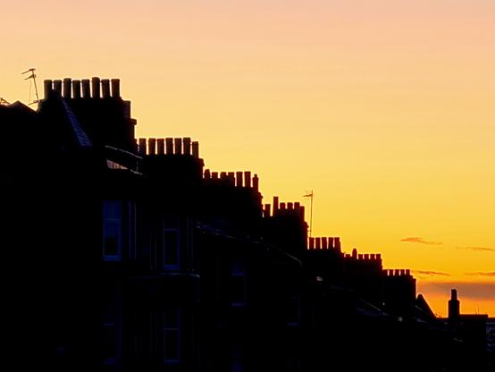 A winter sunrise with tenement chimneys silhouetted against it.
