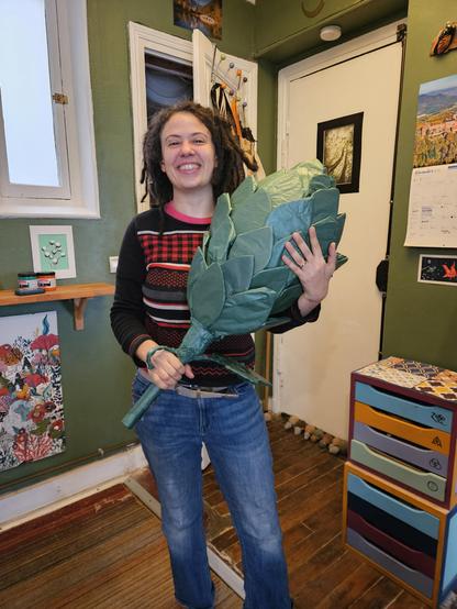 Jaclyn tenant fièrement, comme on tiendrait un bouquet de fleurs, un cône de houblon fait maison d'environ 1 m de long.