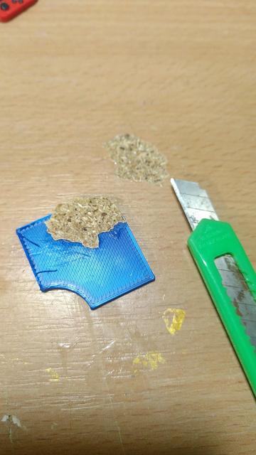 Dasselbe Teil wie zuvor, aber umgedreht. An einer Ecke klebt ein ausgefranstes Stück Spanplatte, darüber das zugehörige Loch in der Tischplatte. Daneben liegt unschuldig ein schmales grünes Stanley Messer mit rostiger Klinge.