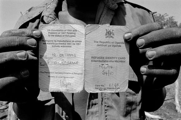 A pair of hands holding an identity card to show to the camera. Text on the card includes 'The Republic of Uganda. Refugee Identity Card'