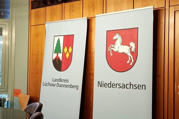 Zwei Banner mit Wappen und Schriftzügen: links Wappen mit Baum und Schrift 'Landkreis Lüchow-Dannenberg', rechts Wappen mit Pferd und Schrift 'Niedersachsen'.