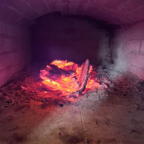 Wood decomposing due to heat in a nest of embers in a combustion chamber of a traditional bricked pizza oven.