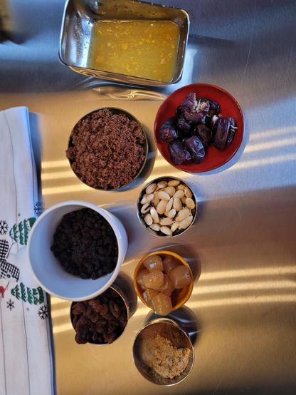 Rvs aanrecht met daarop allerlei bakjes en schaaltjes met daarop dadels, stem gember, amandelen, bruine suiker, kruiden, citroenrasp.