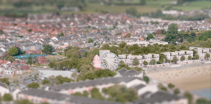 Miniature-style view of Sandy Bay with funfair rides and modern housing.