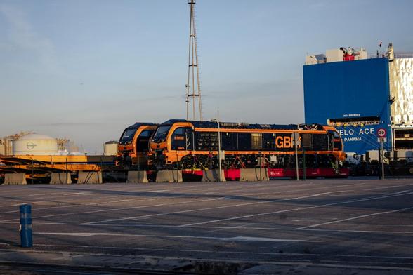 A couple GBRf class 99 locomotives (numbered 99003 and 99004) at a cargo terminal. They have a black livery with an orange outline. The GBRf acronym is on the side of the locomotives.