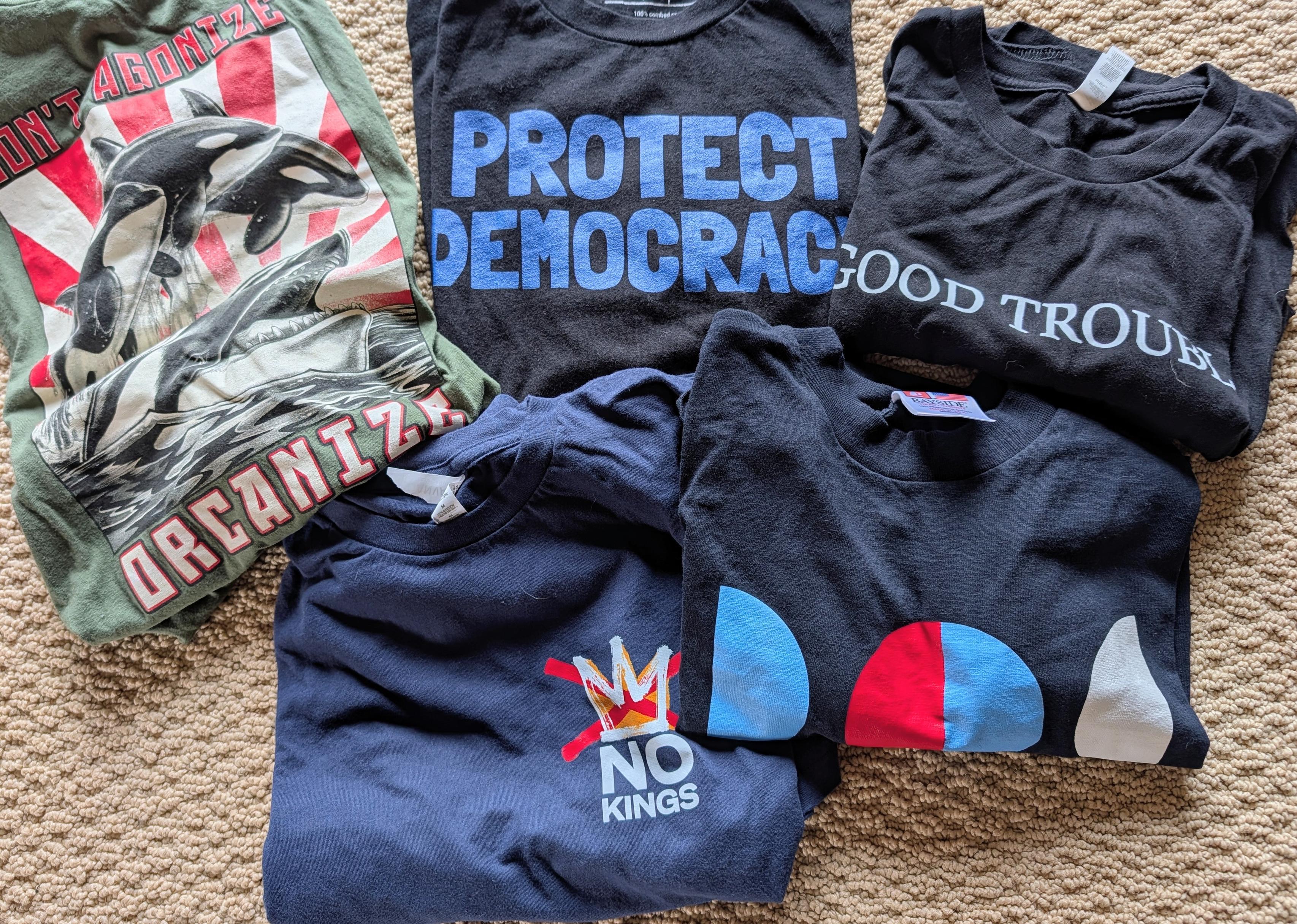 A pile of various resistance themed t-shirts on tan carpet.