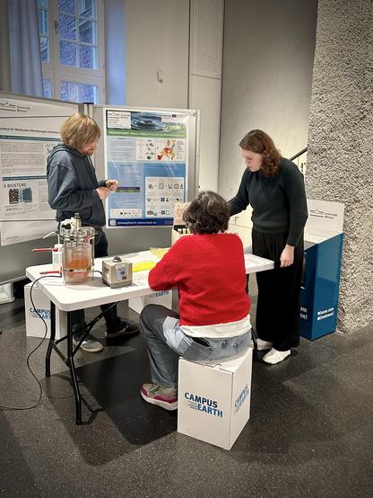 Scientific poster stand with two people presenting a research project on removing pharmaceuticals from wastewater to a third person
