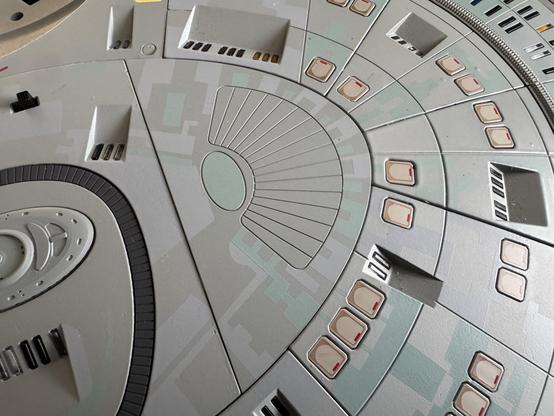 Close-up of a detailed model or replica of a spaceship, featuring various sections with panels, lines, and openings that resemble a sci-fi design.