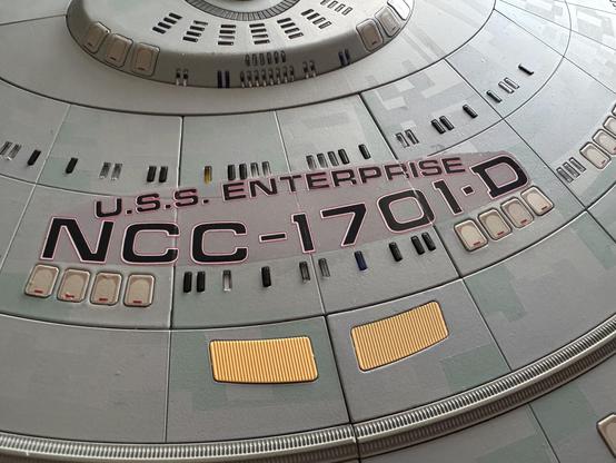 A close-up of a model or replica of the U.S.S. Enterprise NCC-1701-D, featuring detailed markings and panels on its upper surface.