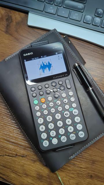 Casio fx-CG100 calculator displaying a 3D graph.  It is resting on a leather covered journal next to a Pelikan M405 fountain pen.