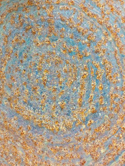 Concentric circles of rust formed by oxidation on a dark iron or steel background. The rust particles bloom in shades of brown, yellow and orange.