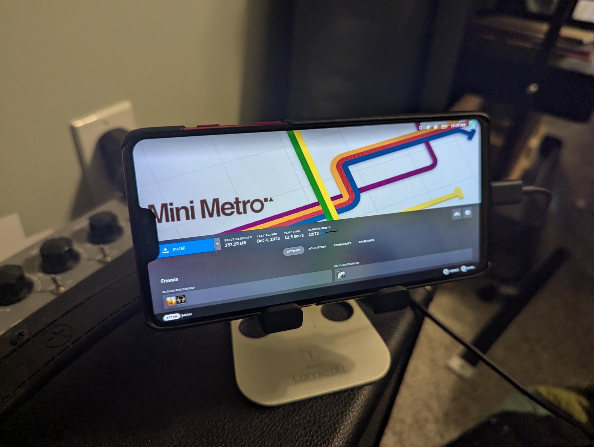 Photo of a phone on a stand running PostmarketOS displaying the Steam Big Picture library page for Mini Metro.