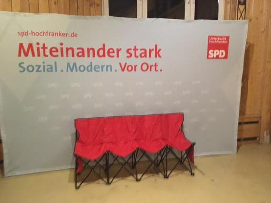 Image-Wand der SPD Hochfranken mit dem Motto "Miteiinander stark. Sozial.Modern.Vor Ort."und roter Sitzgruppe
