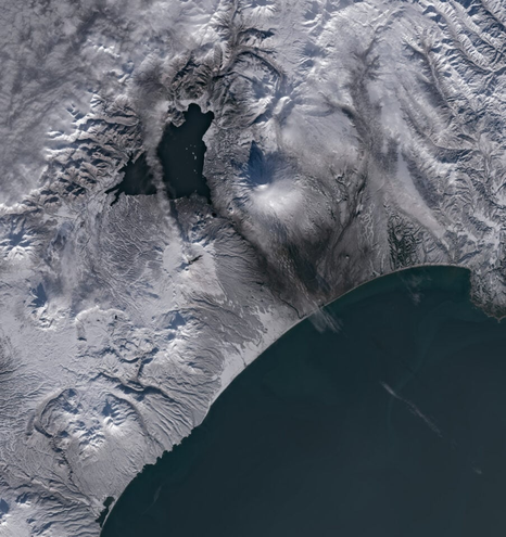 Image satellite montrant la péninsule du Kamtchatka, avec le volcan Krasheninnikova en éruption, émettant un panache dense de cendres au-dessus des paysages enneigés.