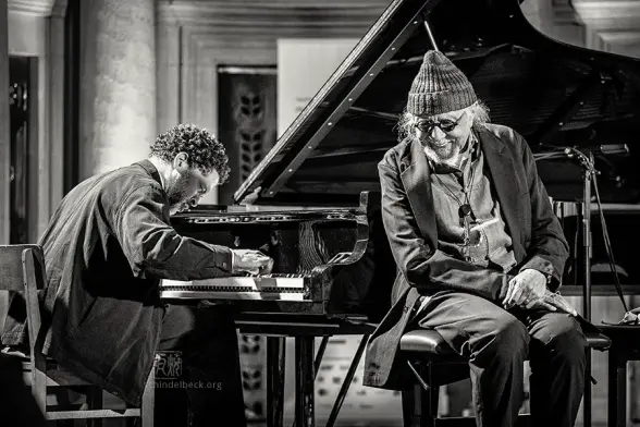Saxophonist und Flötist Charles Lloyd hört sinem Pianisten Jason Moran beim Enjoy Jazz Konzert in der Mannheimer Christuskirche lächelnd und zugwandt zu. Ein Schwarzweißfoto von Frank Schindelbeck Jazzfotografie.