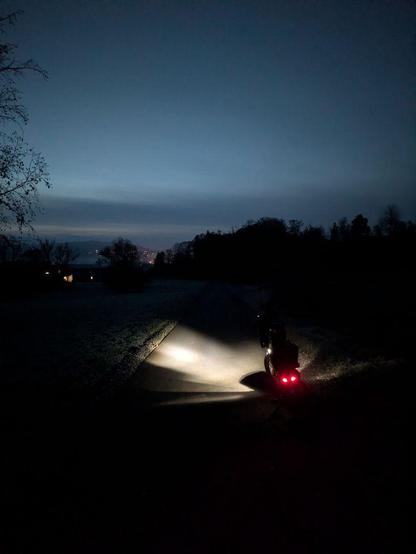 beleuchtetes Fahrrad im Dunklen; im Hintergrund ist das erste zaghafte Morgenlicht am Himmel zu erkennen
