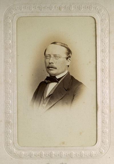 A historical photograph of a man with glasses, dressed in formal attire, featuring a bow tie and a suit jacket.