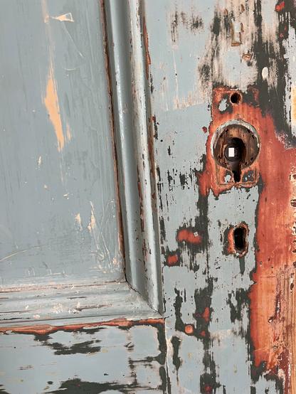 An old door with missing door handles. the door has been sanded down and one can see various colors appear through the layers of paint.