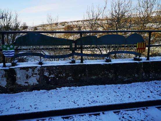A metal sign on the South Tynedale railway about a mile or so from Alston. On the left it says "Cumberland 'and on the right,"Northumberland. " it's a cold day with snow on the ground and the railway is in shade, sun is low, so the photo looks dark.
