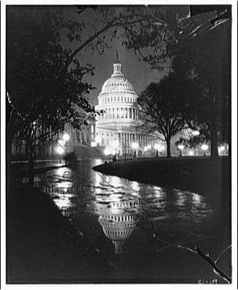 A black and white photograph of the U.S. Capitol building at night, showing its iconic dome illuminated by lights. The reflection in a puddle on the ground creates an almost symmetrical image of the structure, enhancing the visual impact. This photo appears to be from around 1920-1950 based on historical context and stylistic elements such as the quality of black-and-white film used during that era.

This photograph is part of a collection by Theodor Horydczak (approximately 1890-1971), who was known for his architectural photography, often capturing significant buildings in Washington D.C. It's likely to be an older print or reproduction given the provided historical context and website source information.

The image is credited with a reference number "C_42/1" which suggests it might belong to a larger collection of photographs by Horydczak depicting various Capitol exteriors captured around that time period (ca. 1920-ca. 1950).