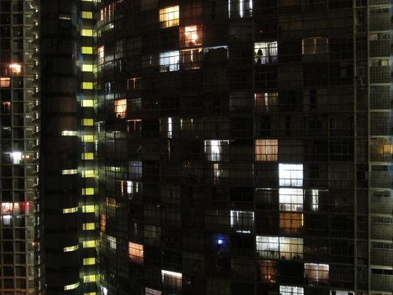 vue nocturne de la façade ondulée d'un immeuble. De nombreuses fenêtres sont obscures, mais certaines sont éclairées de l'intérieur.