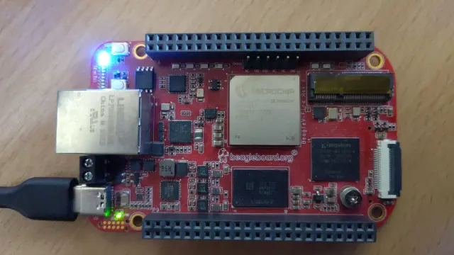 A picture of a BeagleV-Fire board connected to a USB-C cable and with lit up blue and green LEDs.