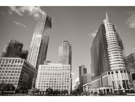 Sepia-toned photo of a modern city skyline with tall, diverse architectural buildings. The scene conveys a sense of urban sophistication and grandeur.