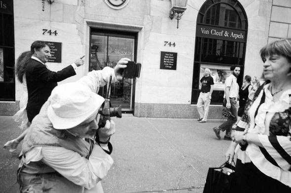 A photo of Bruce Gilden doing the dick move of shooting a portrait (not asked for) up close with a wide angle lens and a flash to the face. Taken from some documentary about him, or a workshop, idk