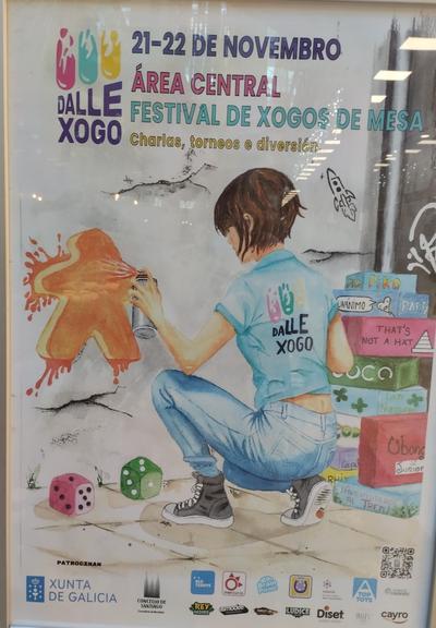 Cartaz da feira de jogos de mesa Dalle Xogo. A ilustração é uma moça anicada a pintar com spray um meeple laranja em uma parede. Abaixo há dois dados e à sua direita uma torre de caixas de jogos de mesa.