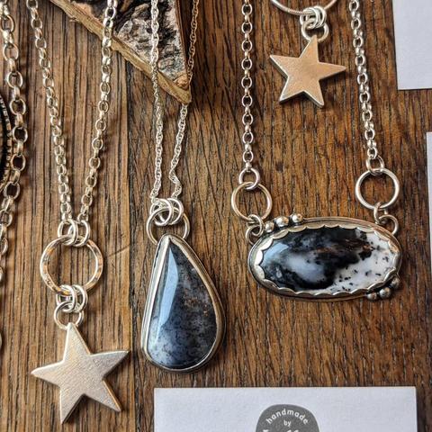 A selection of necklaces on a grained wooden background, featuring solid silver stars and semi-previous black and white stones in sterling silver bezels.