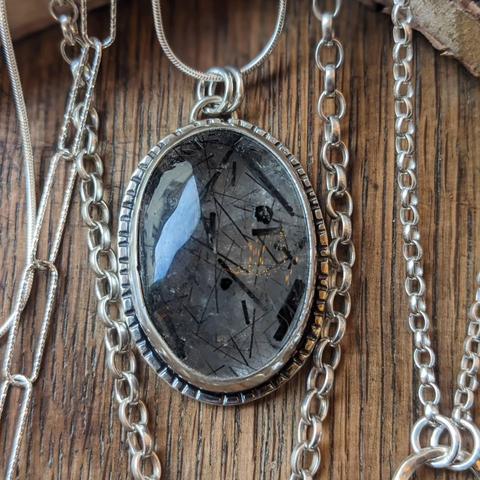 A large dark oval stone with sparkly glints, set in a fancy silver bezel suspended from a silver ring, as part of a necklace