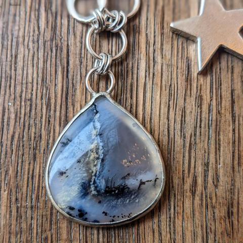 A large dark teardrop stone with sparkly highlights, mounted in a silver bezel suspended from several silver hoops as part of a pendant