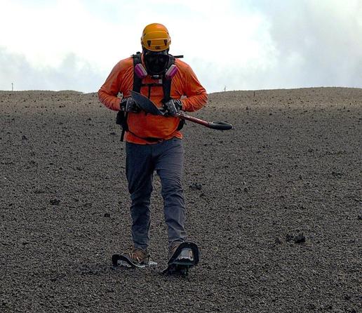 Hawaiian Volcano Observatory field engineers on July 10, 2025, visited monitoring stations downwind of the Kīlauea summit eruptive vents. They wore snowshoes, as the large footprint keeps the field engineers walking on top of the frothy pumice everywhere instead of sinking through it. The mask is necessary due to the sharp tephra shards. (Photo: U.S. Geological Survey/M.Warren)