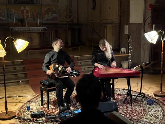 Photo of two people on a stage playing stringed instruments.