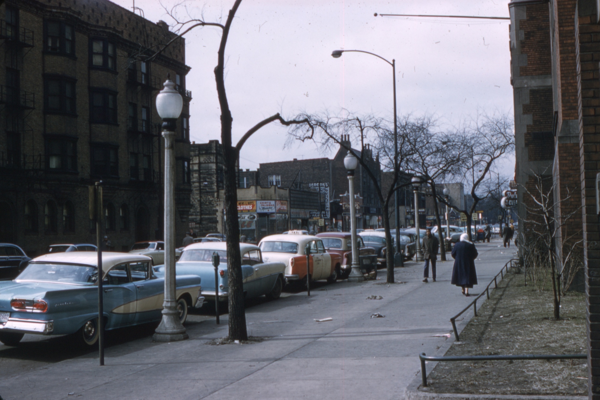 A city street in the States with cars parked along the road. Most likely taken in the 50s.