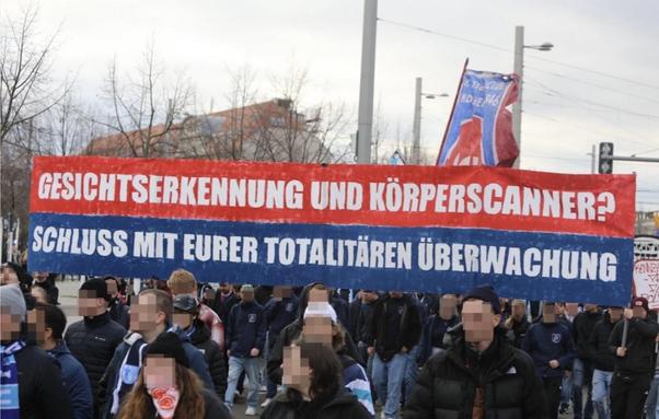 Demoszene zeigt Banner mit dem Schriftzug „Gesichtserkennung und Körperscanner? Schluss mit eurer totalitären Überwachung“