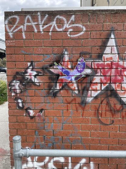 A brick wall with graffiti. A paste-up of a flying purple magpie is in the centre.