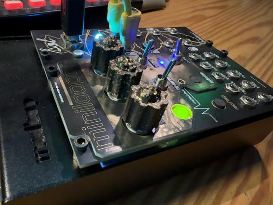 The image features a close-up of synthesizer modules, the "minilooper" and "Sol". It includes control knobs, switches, and various jacks, illuminated by LED lights, set on a wooden surface.