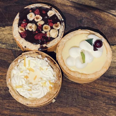 Three small pies with various toppings on a wooden surface.