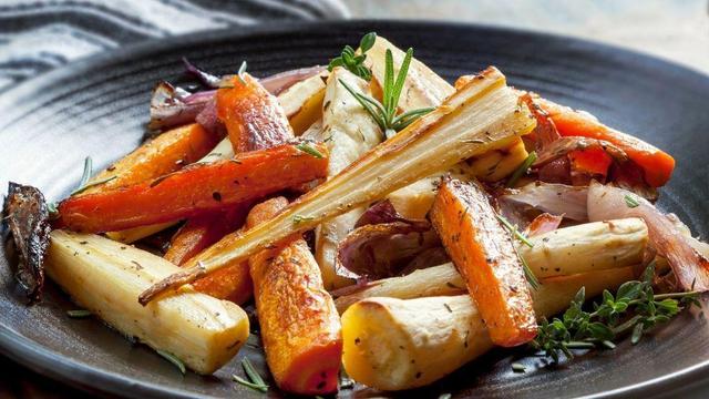 A plate with roasted root vegetables, including carrots, parsnips and red onion, with herbs.