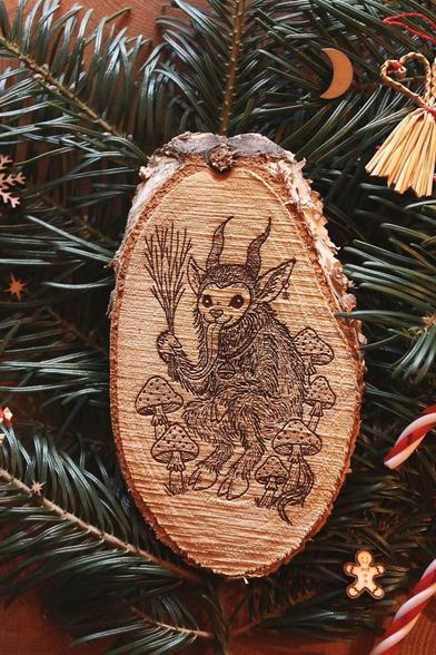 Gebettet auf Tannenzweigen und weihnachtlicher Dekoration liegt in der Mitte eine ovale Birkenholzscheibe mit eingebranntem Bild. Das Motiv zeigt einen Krampus, der zwischen Fliegenpilzen sitzt. Er hat einen Pentagramm-Ohrring am Ohr, eine große Glocke um den Hals und hält eine Rute aus Zweigen in der Klaue.