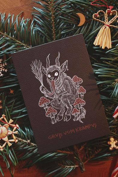 Gebettet auf Tannenzweigen und weihnachtlicher Dekoration liegt in der Mitte eine schwarze Karte mit weiß-rotem Aufdruck. Das Motiv zeigt einen Krampus, der zwischen Fliegenpilzen sitzt. Er hat einen Pentagramm-Ohrring am Ohr, eine große Glocke um den Hals und hält eine Rute aus Zweigen in der Klaue. In roter Schrift steht darunter: Gruß vom Krampus